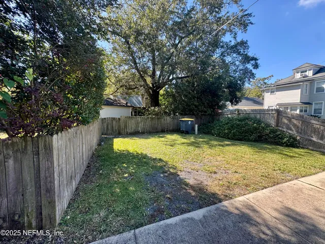 a view of a backyard with large trees and wooden fence