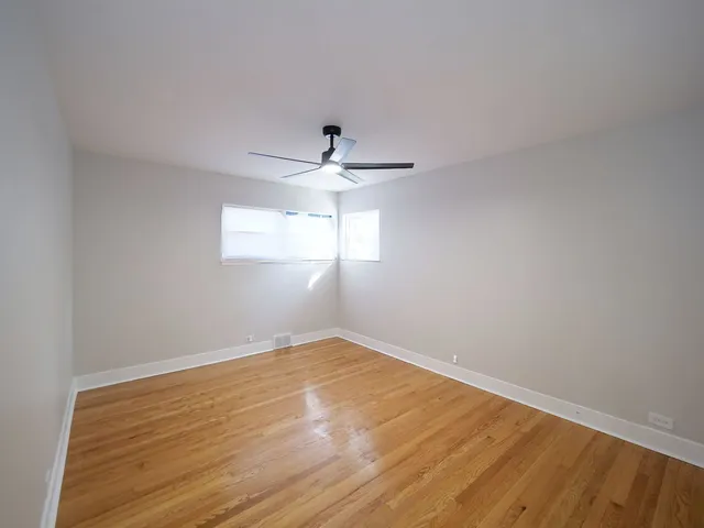 a view of empty room with wooden floor and fan