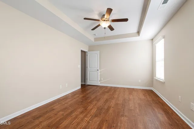 an empty room with wooden floor ceiling fan and windows