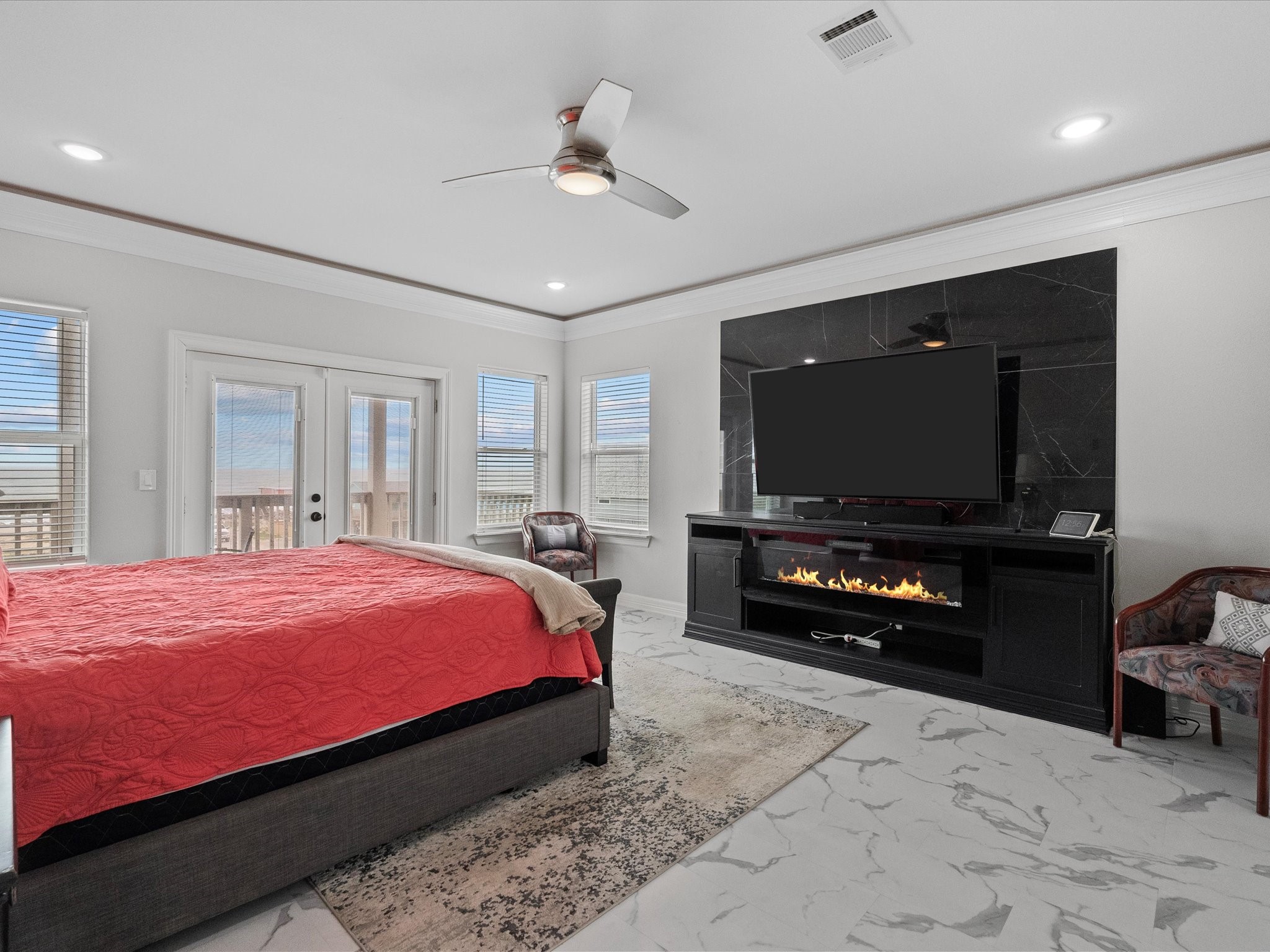 1018 Seashell Drive Surfside Beach, TX 77541 - Photo 40 of 49 This spacious bedroom features a modern design with a cozy fireplace and large TV setup. It has a king-sized bed, elegant marble flooring, and ample natural light from multiple windows and a set of French doors leading to a balcony.