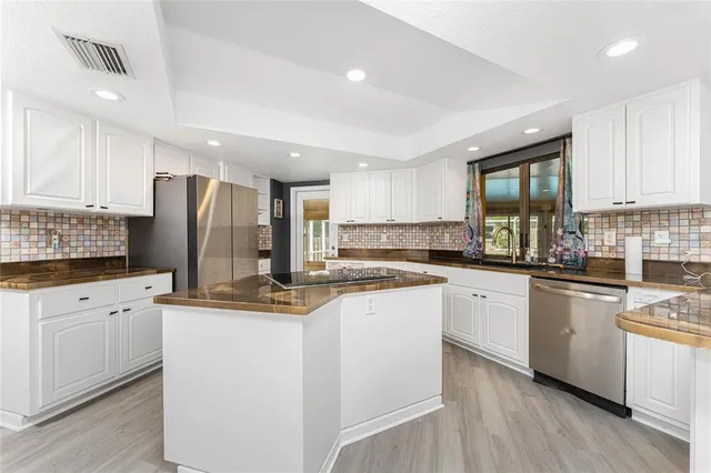 a kitchen with stainless steel appliances granite countertop a refrigerator a sink dishwasher a stove and white countertops with wooden floor