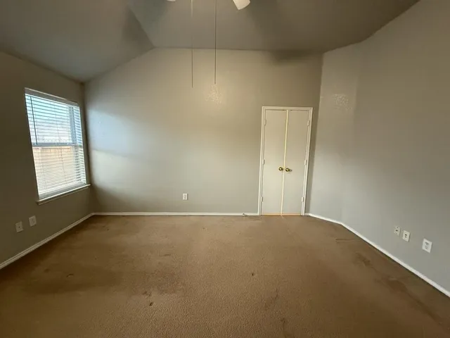 an empty room with a chandelier fan and windows