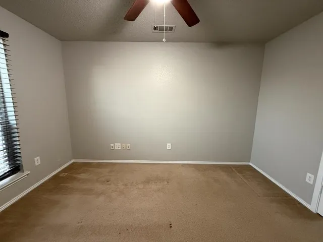 an empty room with a chandelier fan and windows