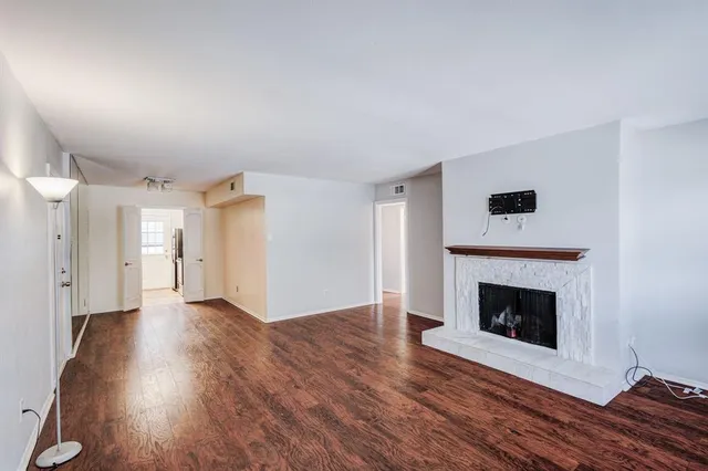 a view of an empty room with wooden floor fireplace and a window