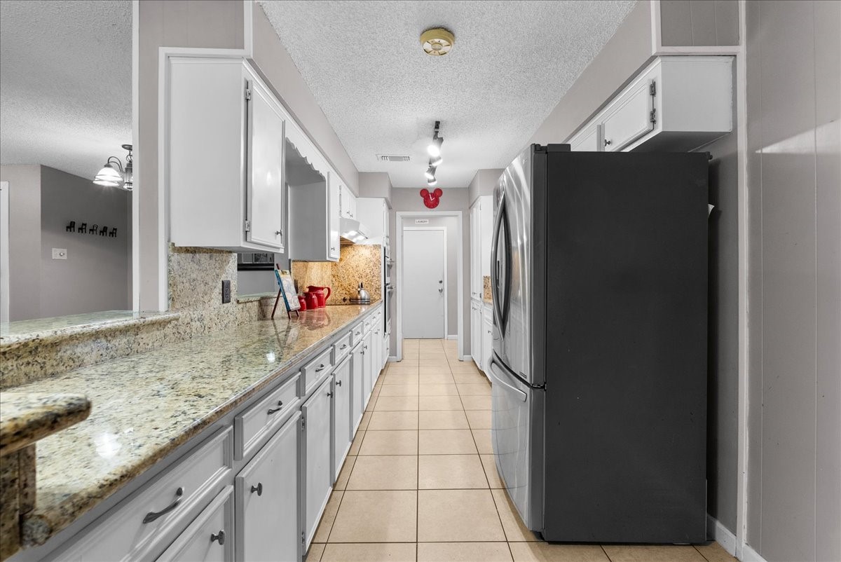 883 Silverpines Road Houston, TX 77062 - Photo 14 of 38 This kitchen features a sleek galley layout with granite countertops, ample cabinetry, and modern stainless steel appliances. The neutral tile flooring complements the space, providing a clean and inviting atmosphere.