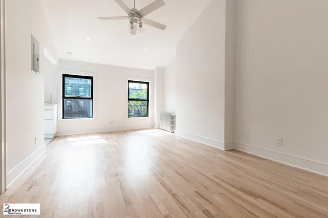 an empty room with wooden floor chandelier fan and windows