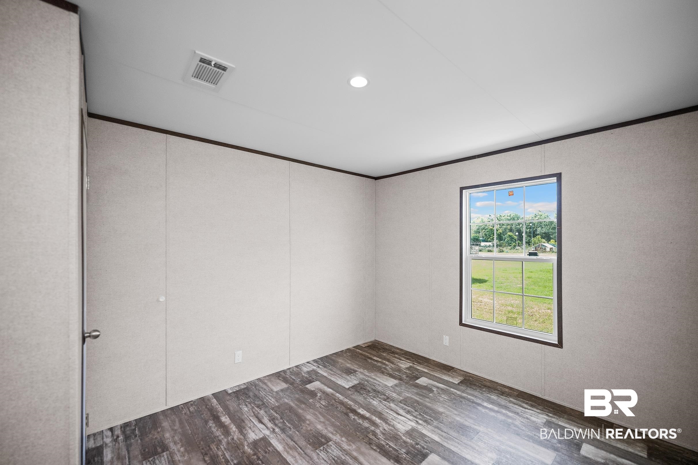 21601 Westside Loop Silverhill, AL 36576 - Photo 34 of 42 Room featuring wood-finish flooring, a single window with a dark frame, light-toned panel walls, dark trim, and a ceiling-mounted recessed light