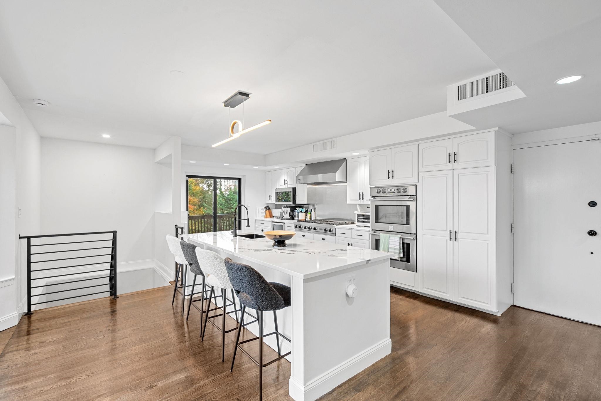 76 Hackensack Plank Road Weehawken, NJ 07086 - Photo 15 of 44 a kitchen with stainless steel appliances kitchen island granite countertop a stove a refrigerator a dining table and chairs with wooden floor