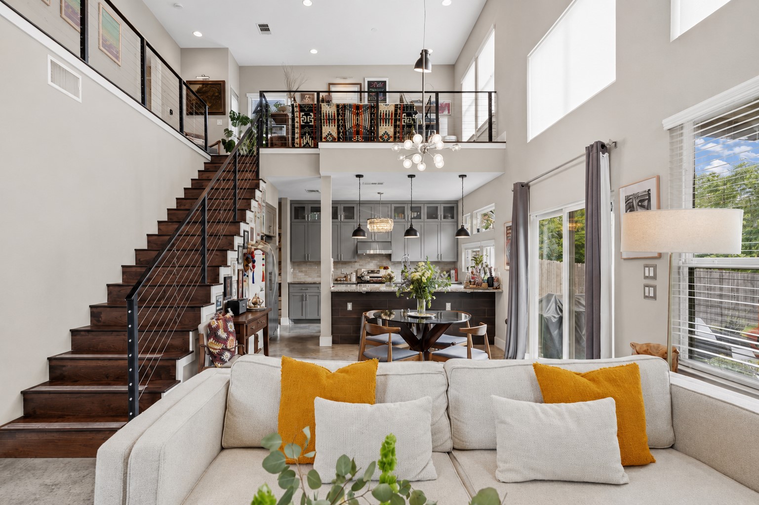 1800 Webberville Road, Unit B Austin, TX 78721 - Photo 7 of 30 Open-concept living space featuring high ceilings, a contemporary kitchen with grey cabinetry and dark island, wood-finish flooring on the stairs and loft, and a prominent staircase with cable railings