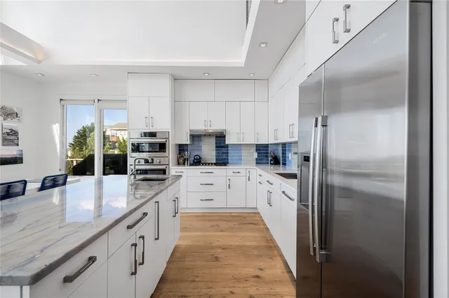 a large kitchen with granite countertop a refrigerator a sink a stove and white cabinets