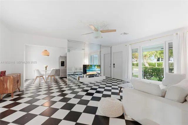 a living room with a black white checkered floor with a gaming machine and dining chairs