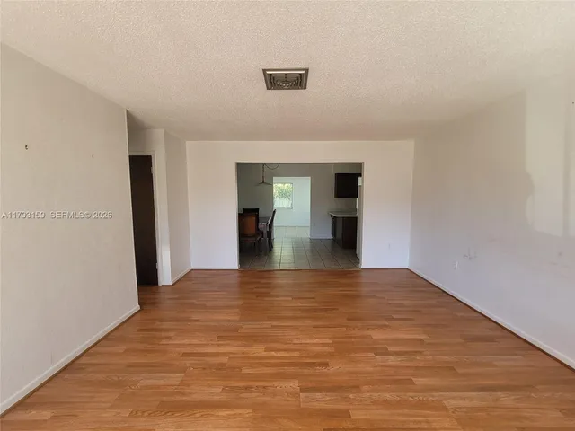 a view of empty room with wooden floor and kitchen view