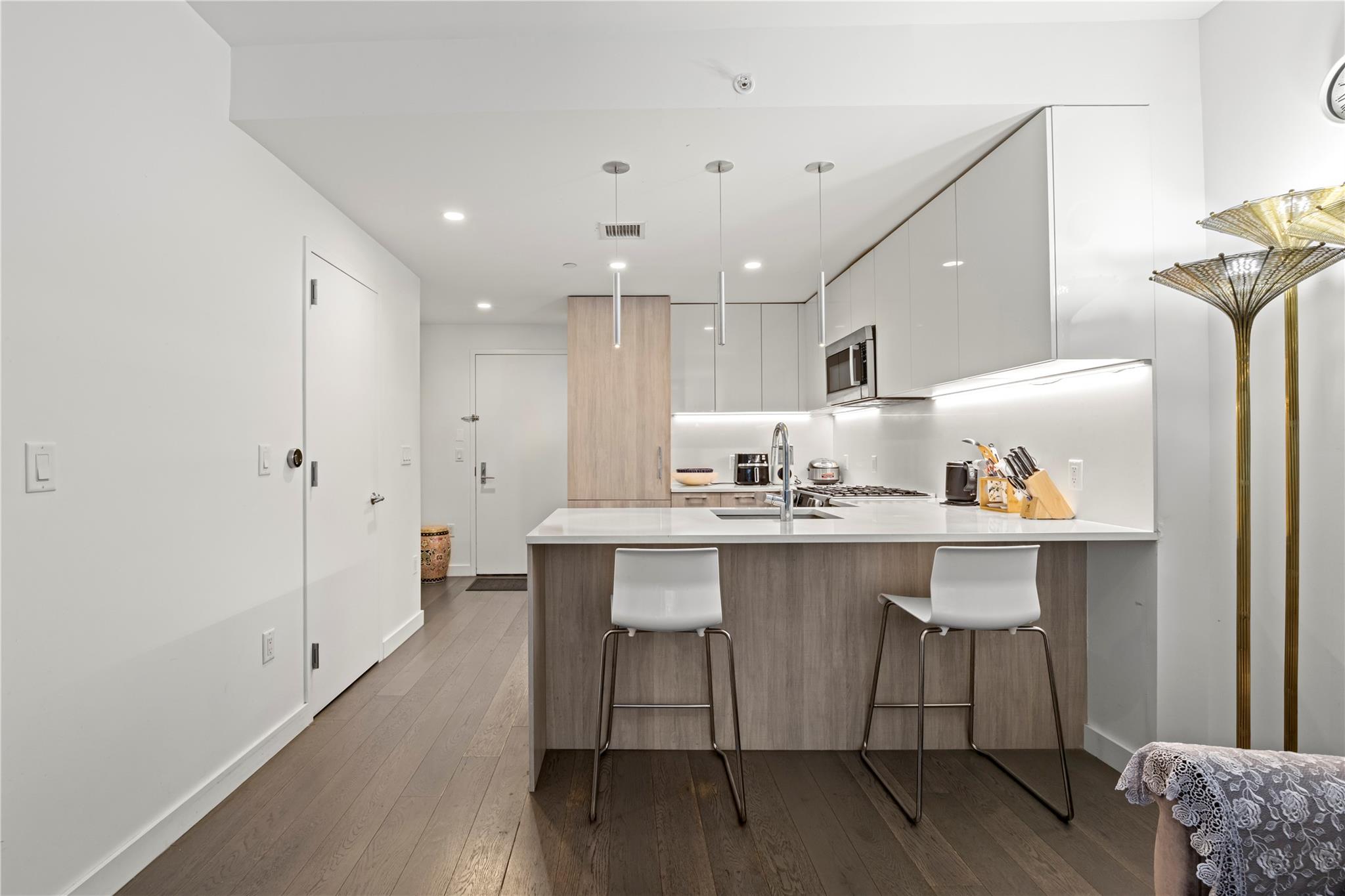 131-05 40 Road, Unit 11M Queens, NY 11354 - Photo 14 of 24 Kitchen with modern cabinets, a peninsula, dark wood-style floors, white cabinetry, and light countertops