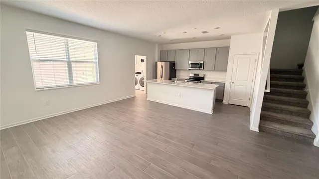 a living room with stainless steel appliances kitchen island wooden floor and window