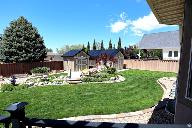 1055 North 1000 East Mapleton, UT 84664 - Photo 72 of 112 Expansive backyard featuring a lush lawn, two storage sheds with dark roofs, a decorative rock garden with plantings, and a full privacy fence