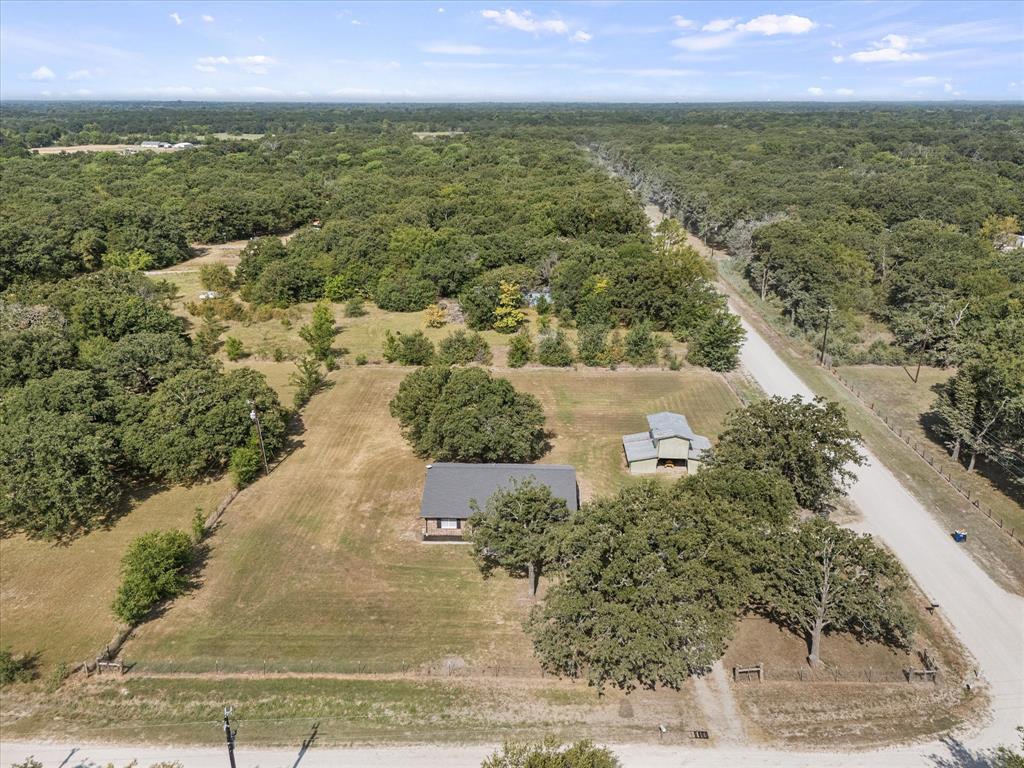 1547 Magnolia Lane Wills Point, TX 75169 - Photo 20 of 22 Expansive wooded surroundings with a gravel road, two distinct structures, and a clear sky overhead