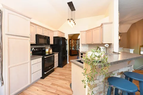 a kitchen with stainless steel appliances kitchen island granite countertop a refrigerator a stove top oven a sink dishwasher and a dining table with wooden floor