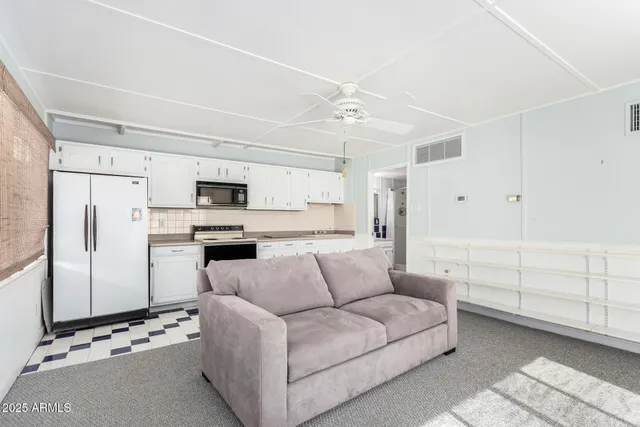 a living room with furniture a refrigerator and white cabinets