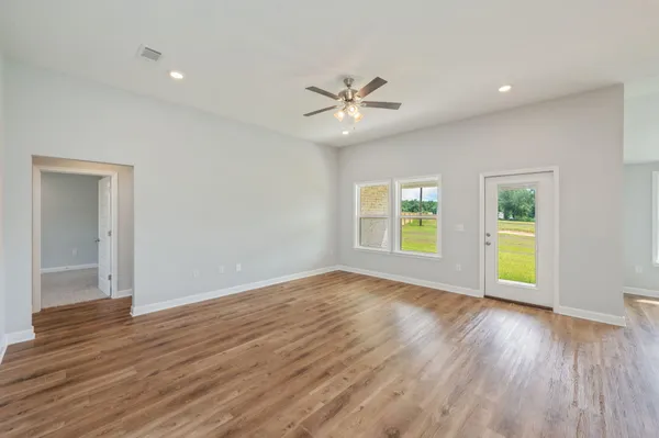 an empty room with wooden floor chandelier fan and windows