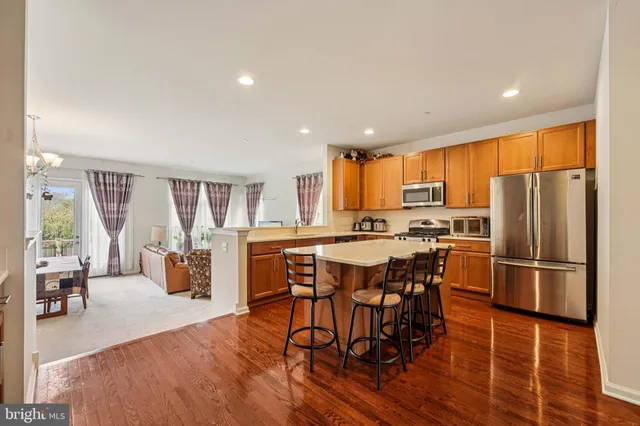 a kitchen with stainless steel appliances a refrigerator a stove a dining table and chairs with wooden floor