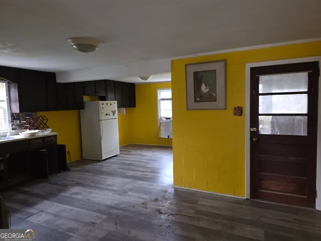 a view of a refrigerator in kitchen and an empty room with wooden floor windows