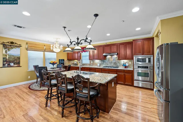 a kitchen with stainless steel appliances kitchen island granite countertop a table chairs and a refrigerator