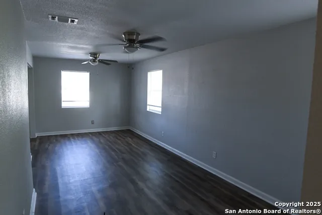 an empty room with wooden floor fan and windows