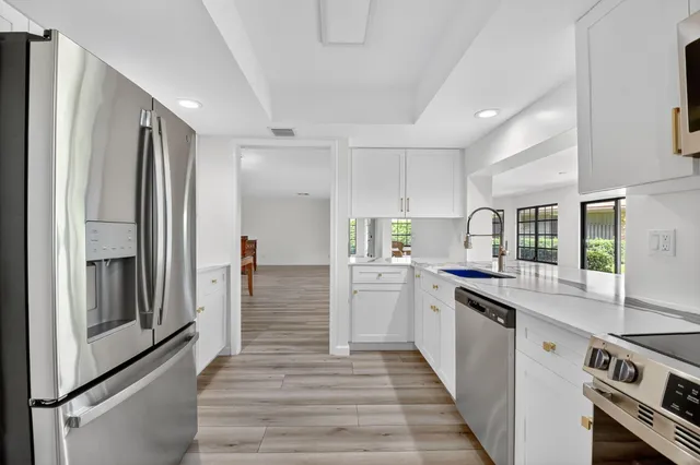 a large white kitchen with stainless steel appliances granite countertop a stove and a sink