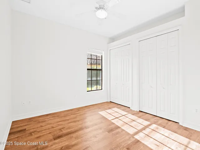 an empty room with wooden floor chandelier fan and windows