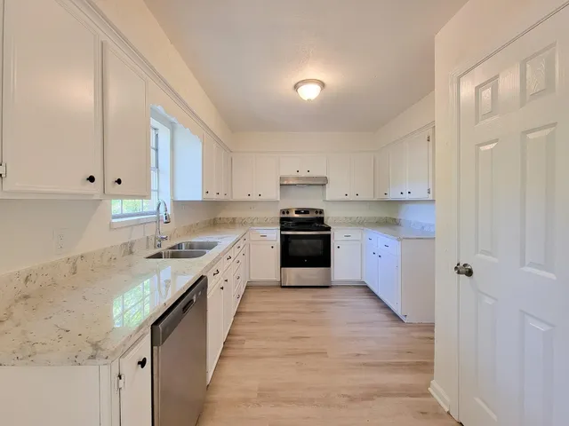 a large kitchen with stainless steel appliances granite countertop a stove top oven a sink dishwasher and a refrigerator with wooden floor