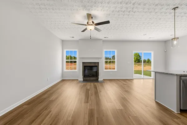 an empty room with wooden floor a ceiling fan a fireplace and windows