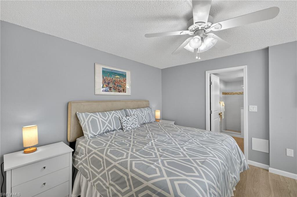 5900 Bonita Beach Road Southwest, Unit 1602 Bonita Springs, FL 34134 - Photo 12 of 26 Bedroom featuring ensuite bathroom, light wood-style floors, a textured ceiling, and a ceiling fan