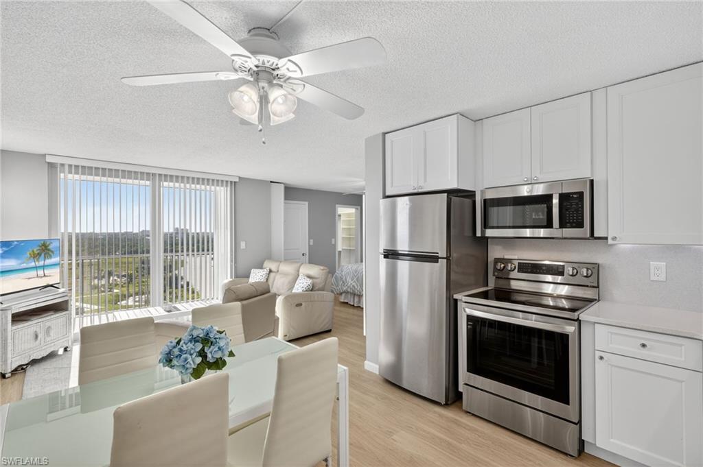 5900 Bonita Beach Road Southwest, Unit 1602 Bonita Springs, FL 34134 - Photo 9 of 26 Kitchen featuring stainless steel appliances, white cabinets, light wood-style flooring, a textured ceiling, and light stone counters