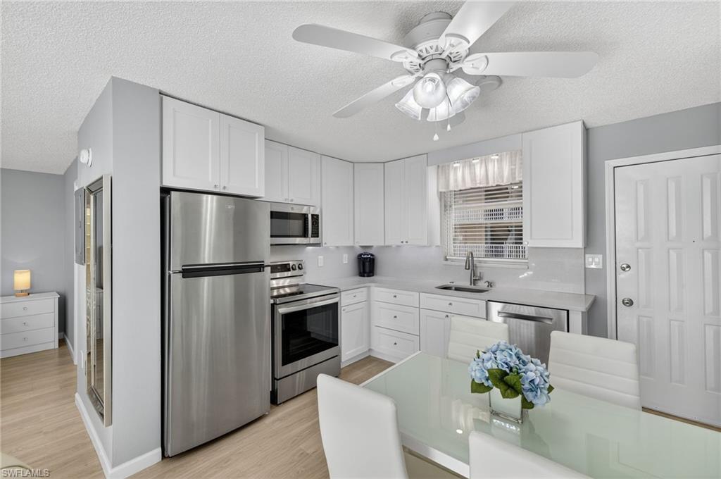 5900 Bonita Beach Road Southwest, Unit 1602 Bonita Springs, FL 34134 - Photo 10 of 26 Kitchen featuring stainless steel appliances, a textured ceiling, white cabinetry, light wood-type flooring, and ceiling fan