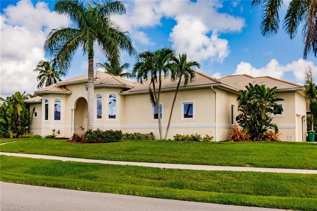 a front view of yellow house with small garden and palm trees