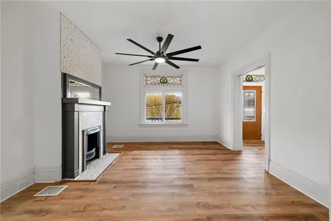 a view of a livingroom with a fireplace a ceiling fan and wooden floor