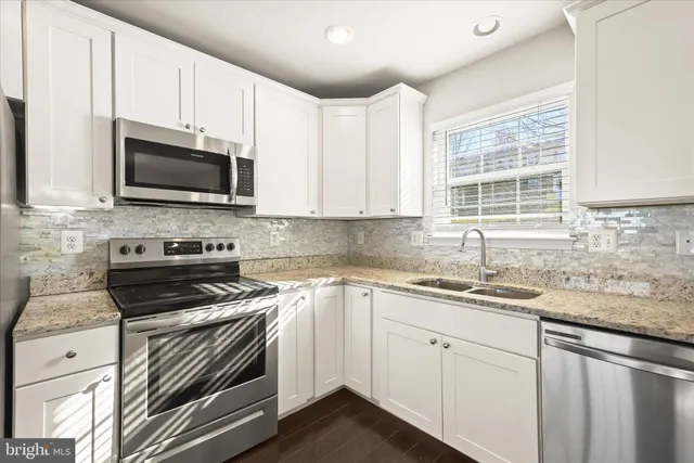 a kitchen with granite countertop a sink dishwasher a stove and a microwave oven with cabinets