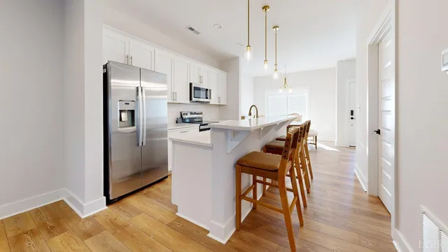 a kitchen with stainless steel appliances a refrigerator a sink dishwasher a stove and white cabinets with wooden floor