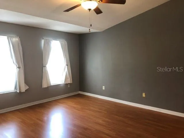 an empty room with wooden floor chandelier fan and windows
