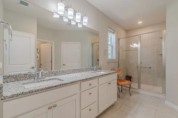 a bathroom with a granite countertop double vanity sink a mirror and a shower