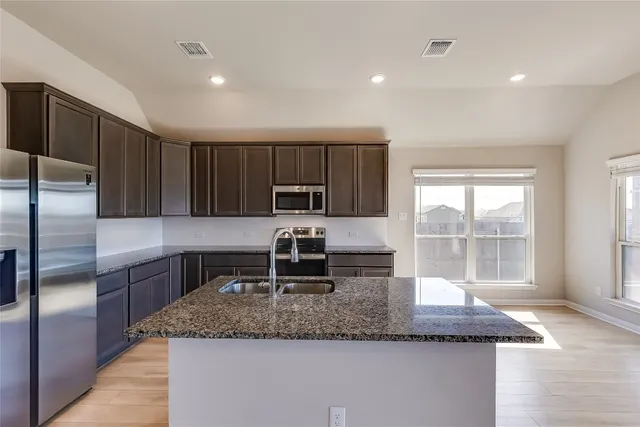 a kitchen with kitchen island granite countertop a sink a counter top space appliances and cabinets
