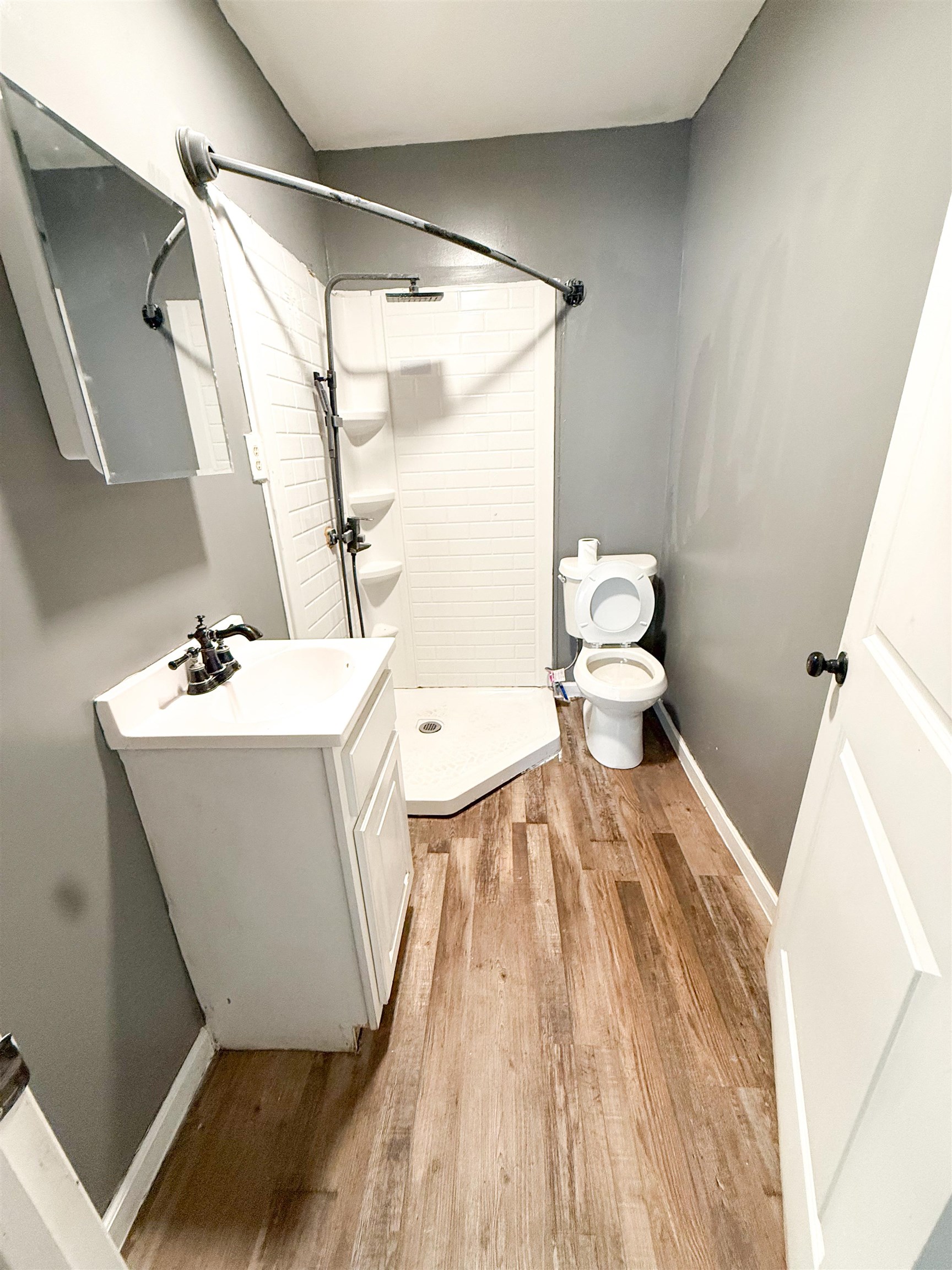 403 Sharp Street Corinth, MS 38834 - Photo 7 of 9 Wood-finish flooring with a corner shower stall, white vanity, and wall-mounted mirror