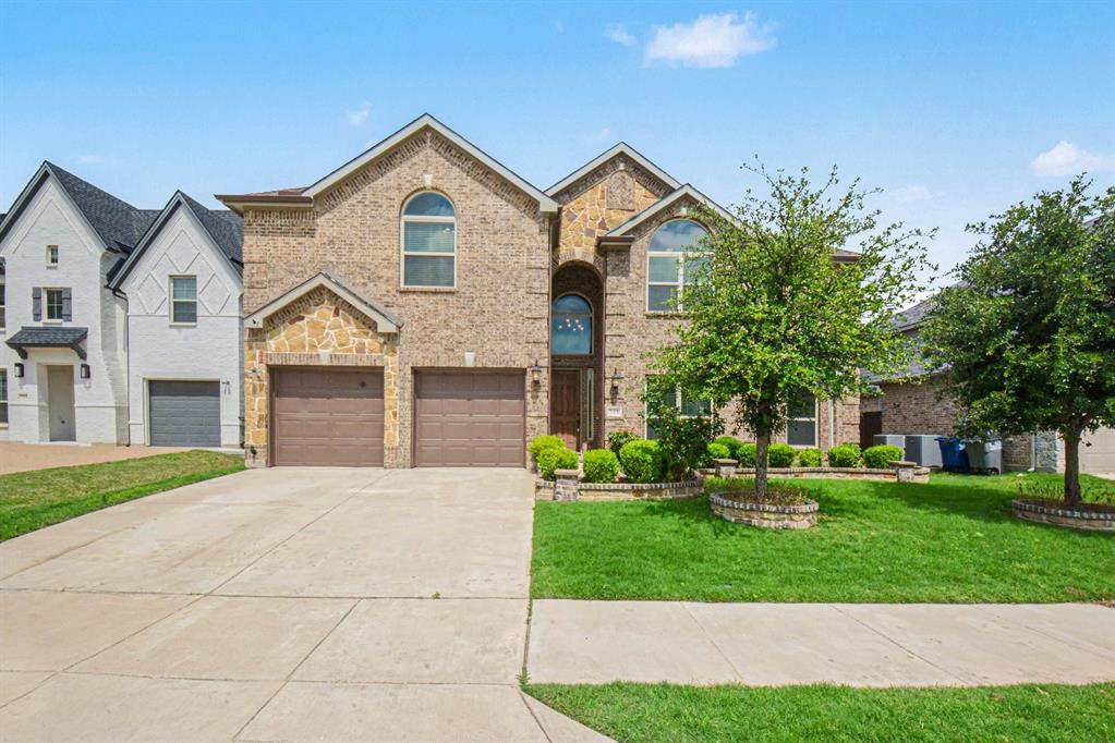 Two-story residence featuring a brick and stone facade, arched windows, a two-car garage, and a concrete driveway