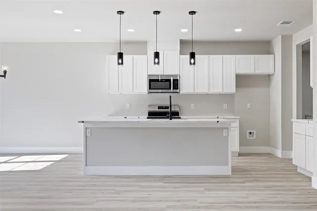 a view of a kitchen with stainless steel appliances granite countertop a stove a sink and white cabinets