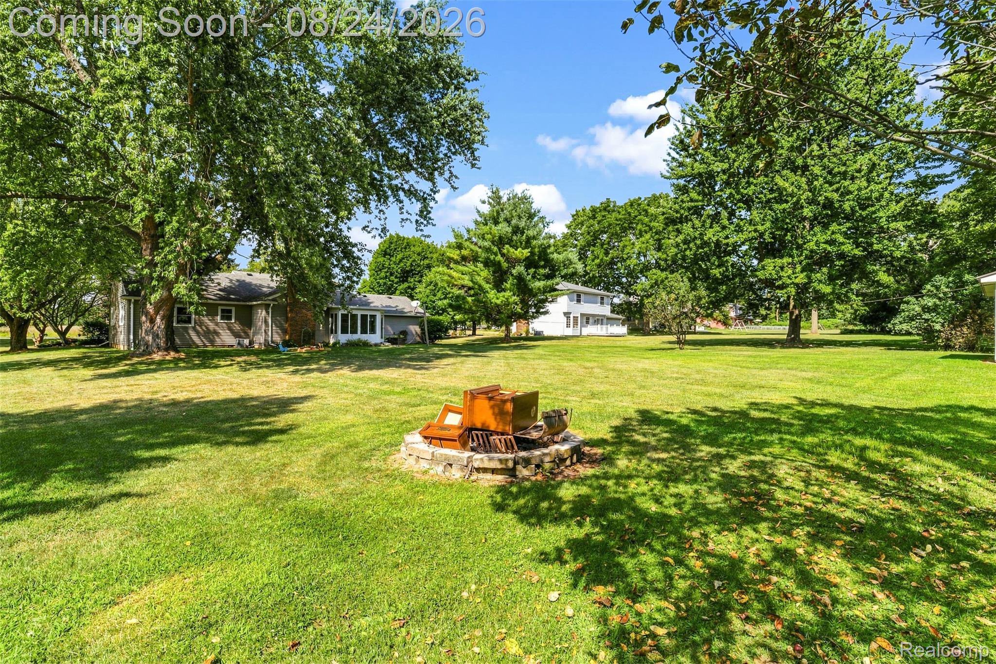 2310 Peppermill Road Lapeer, MI 48446 - Photo 31 of 35 Expansive grassy yard with mature trees, a stone fire pit, and a single-story residence featuring a sunroom addition and wood siding