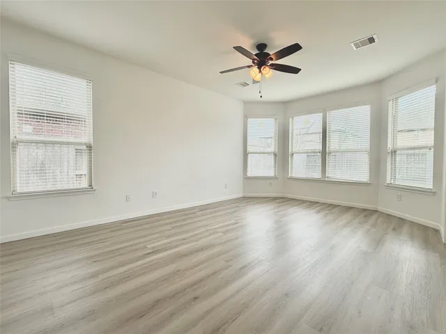 an empty room with wooden floor fan and windows