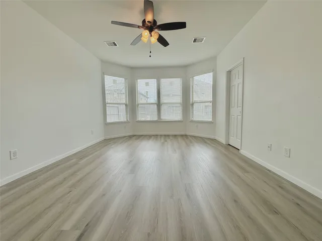 an empty room with wooden floor ceiling fan and windows