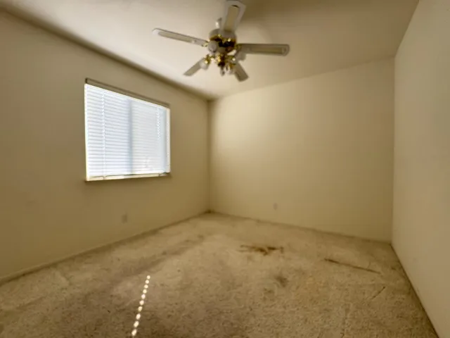 an empty room with a chandelier fan and windows