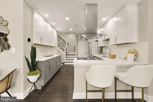 an open kitchen with kitchen island granite countertop a stove a sink a dining table and chairs with wooden floor