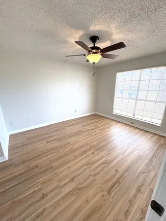 an empty room with wooden floor fan and windows